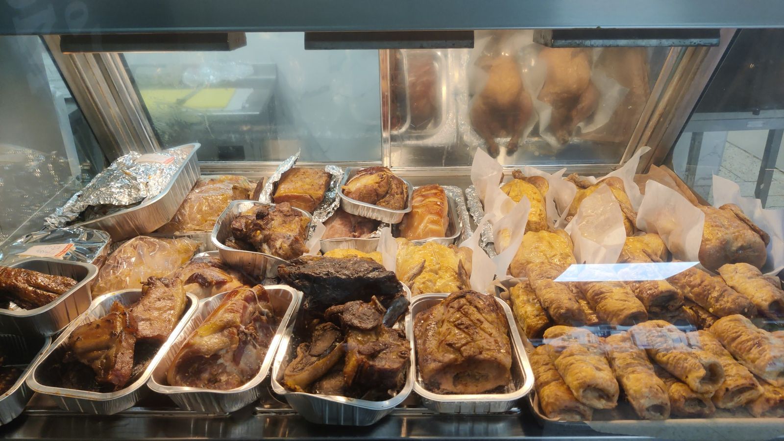Cooked meats cabinet with roast chickens, cooked joints in foil trays and sausage rolls