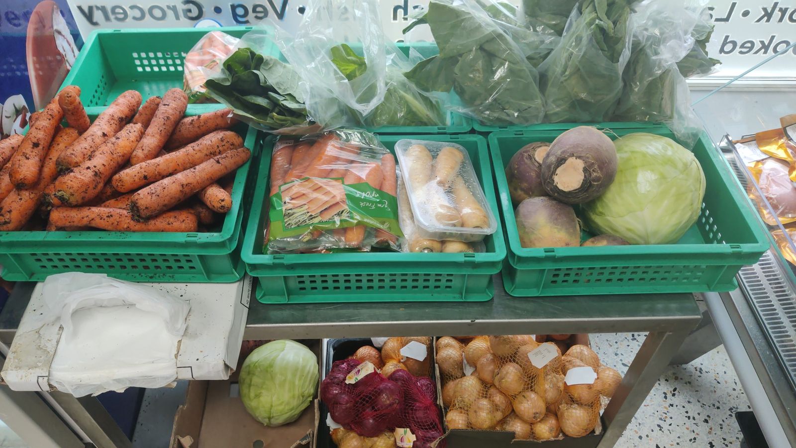 Green crates of fresh carrots, turnips, cabbage, greens and bags of onions